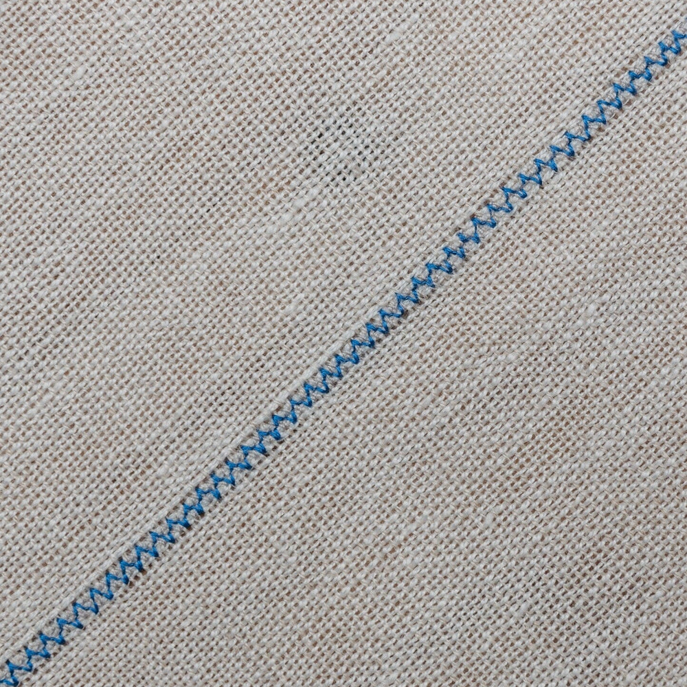 
                  
                    Detalle de mantel artesanal de lino blanco con uniones azules, hecho a mano en España por ÁBBATTE
                  
                