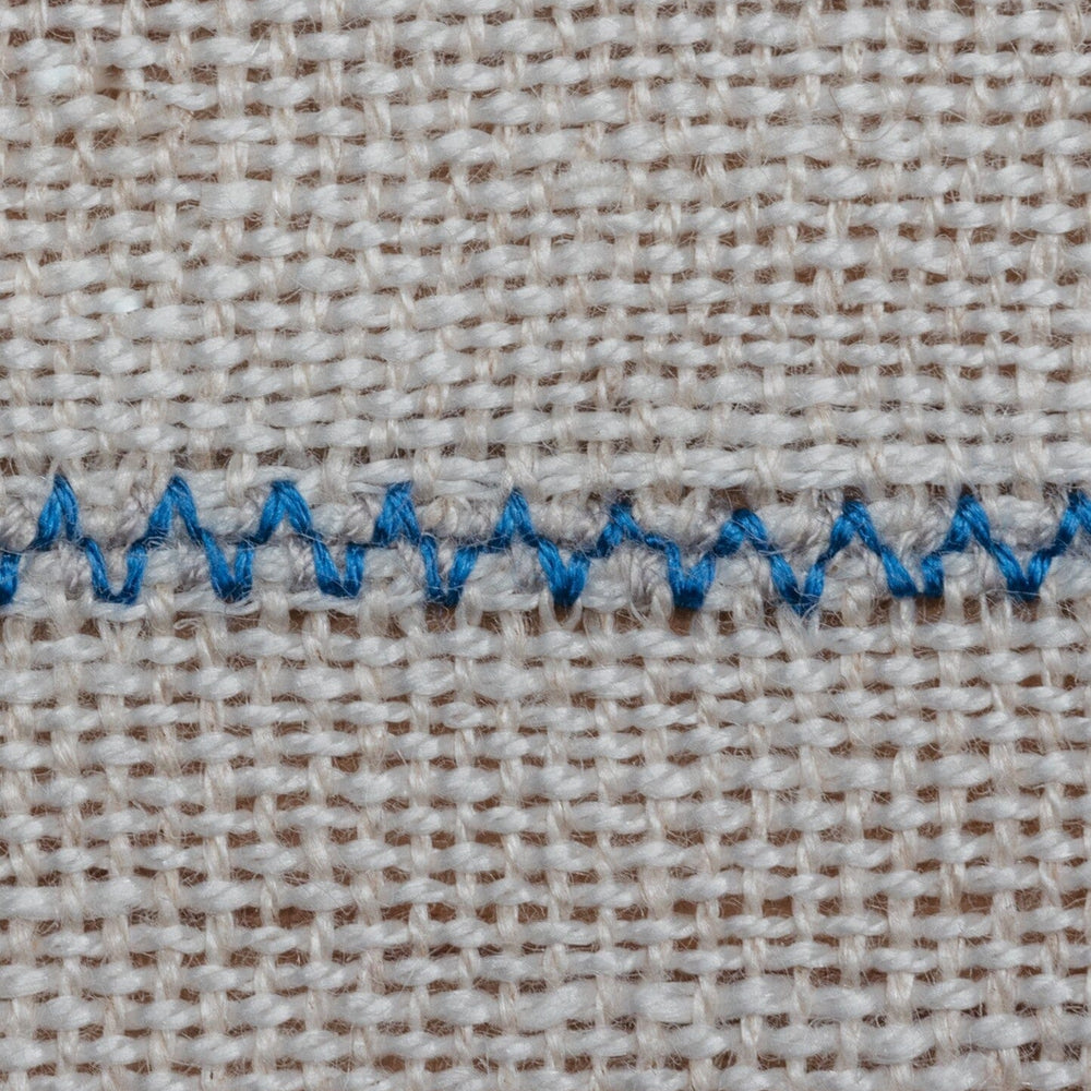 
                  
                    Detalle de mantel artesanal de lino blanco con uniones azules, hecho a mano en España por ÁBBATTE
                  
                